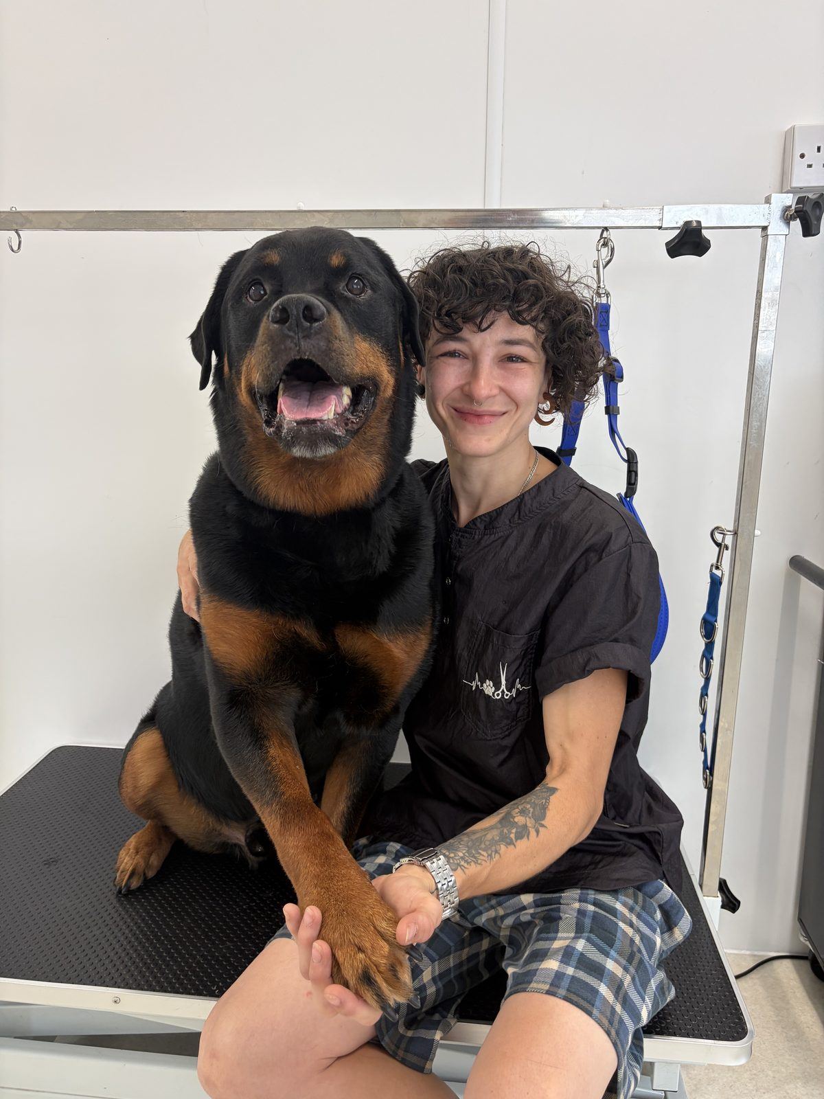 Amber-Louise Brandom sitting on the grooming table with her Rottweiler Mojo, one arm around him and holding his paw